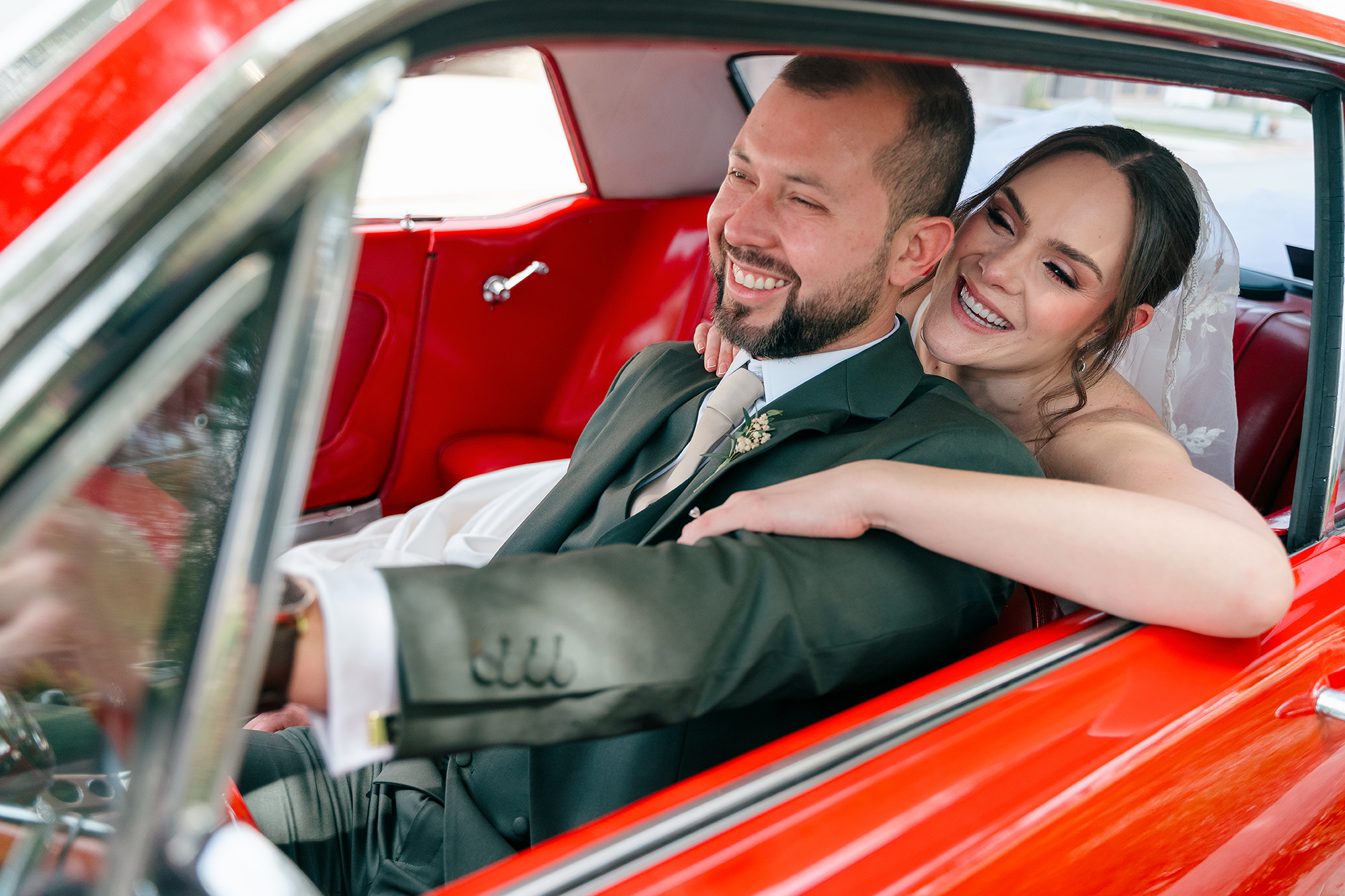 Candid couple portrait in vintage red car — natural laughter, unscripted connection, destination wedding photography