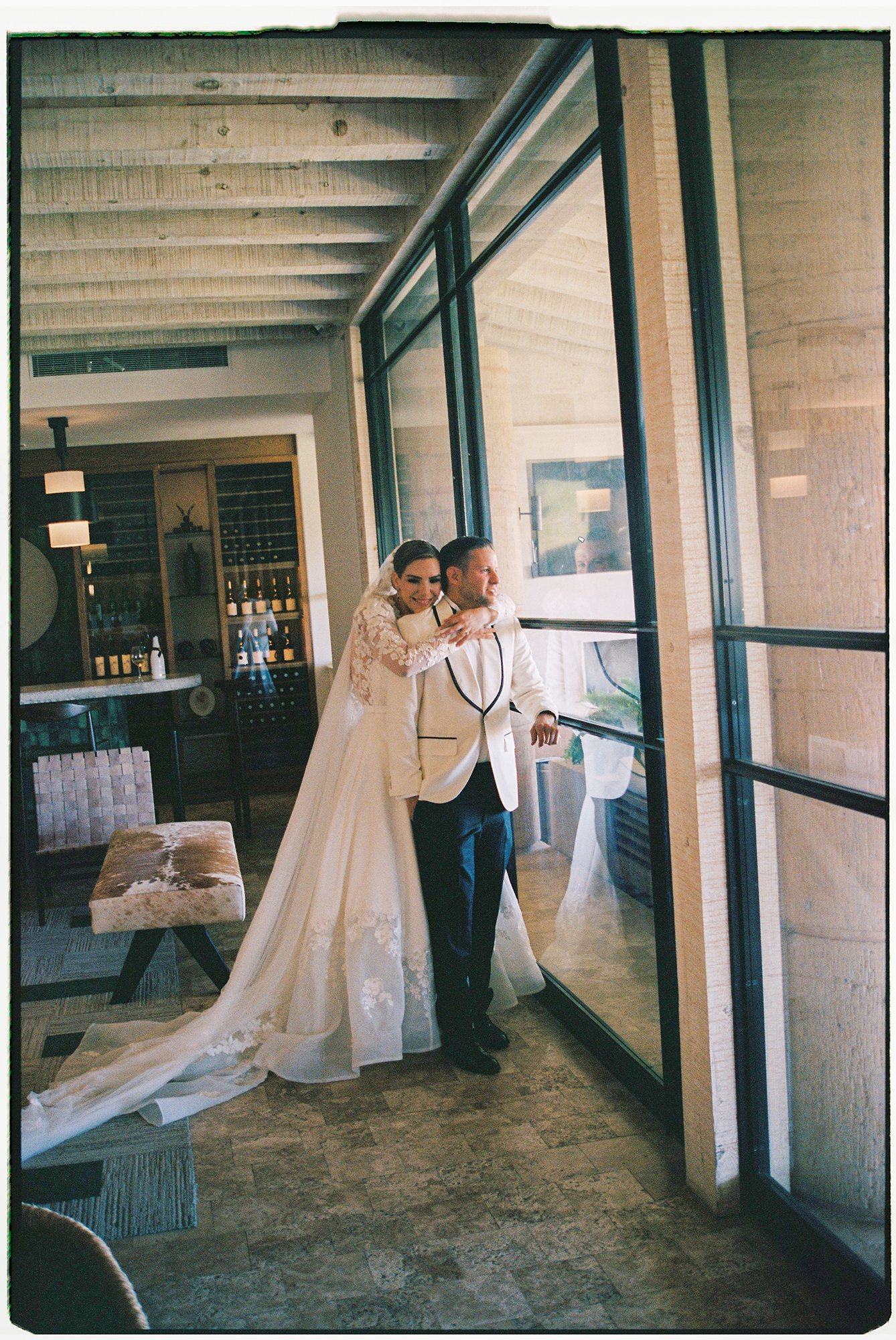 Bride embracing groom by a steel-framed window, natural light on 35mm film — David Lack