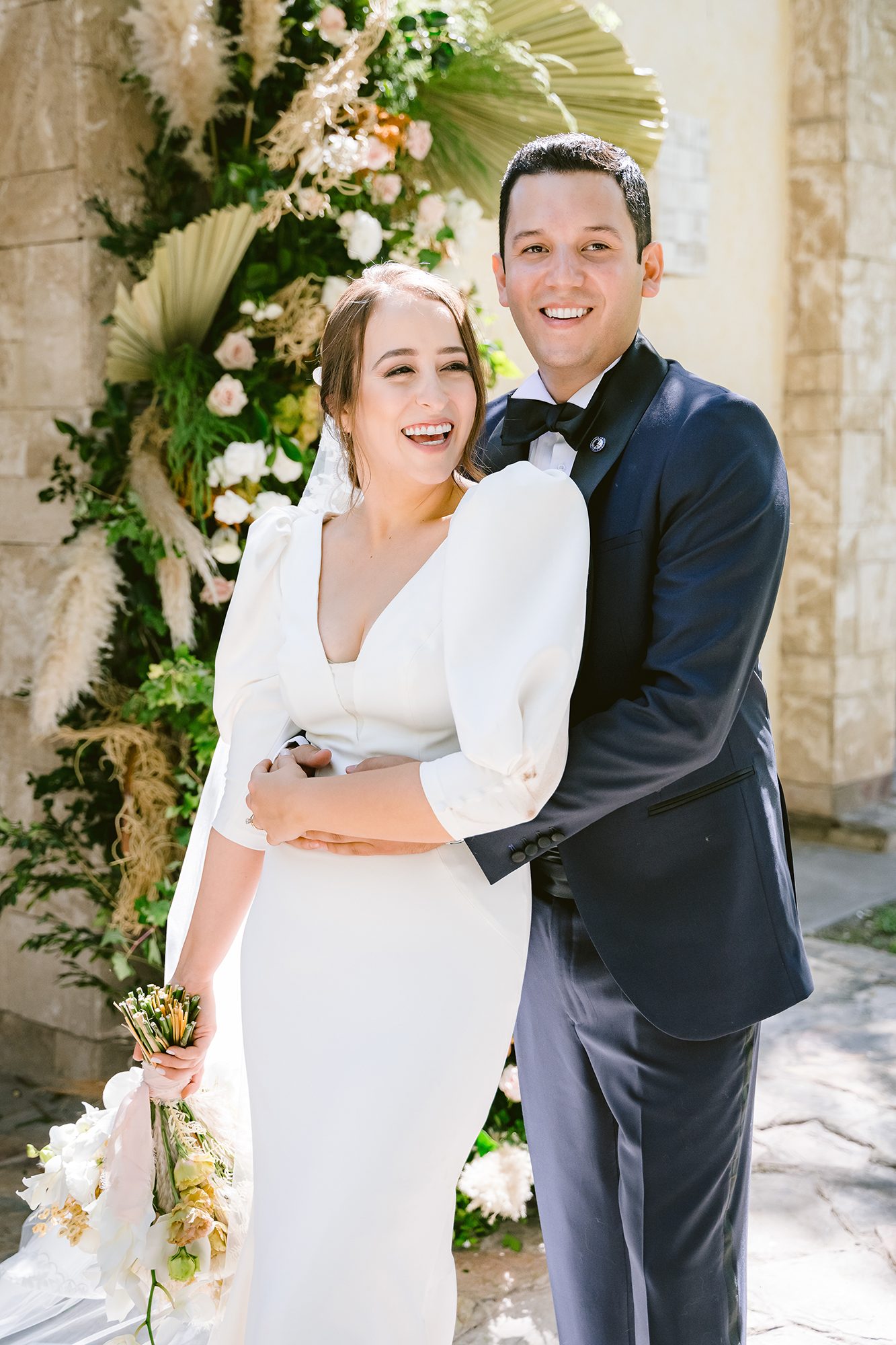 María riendo abiertamente junto a Gilberto frente al arco floral — fotografía tomada por su papá, David Lack