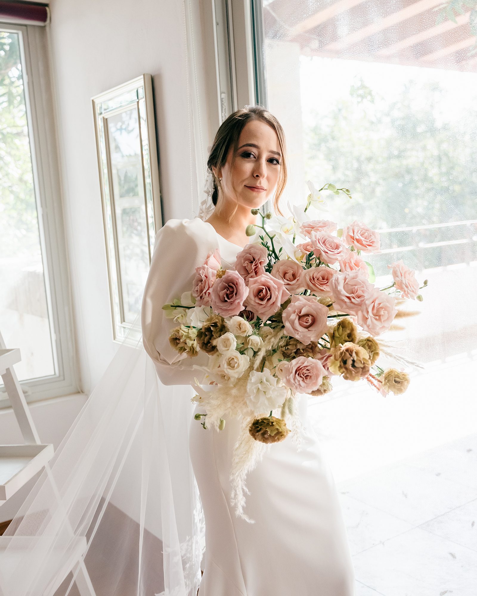 María sosteniendo su ramo de rosas y orquídeas junto a la ventana mientras se prepara