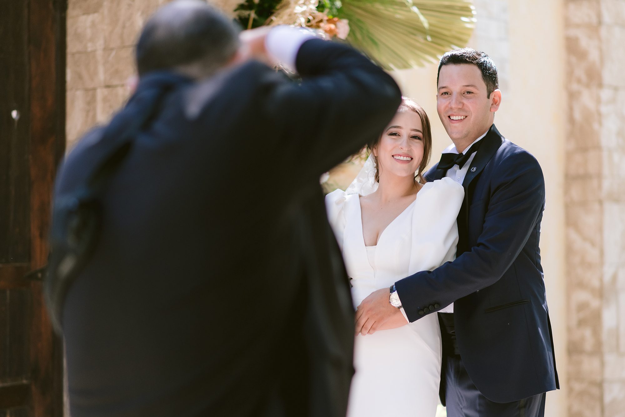 El papá de la novia, David Lack, fotografiando a los novios, visto de espaldas con la cámara arriba mientras María y Gilberto sonríen a su lente