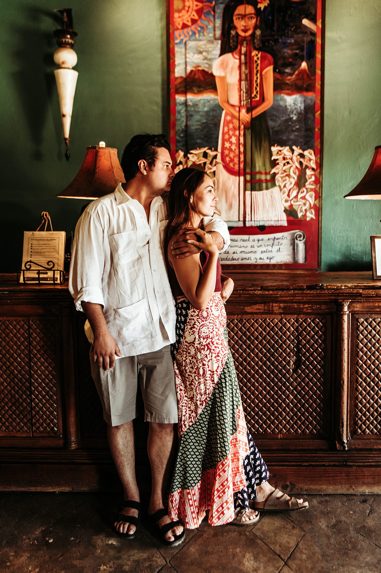 Couple embracing in a historic Todos Santos hotel lobby beneath Mexican folk art — destination couple photography Baja California Sur
