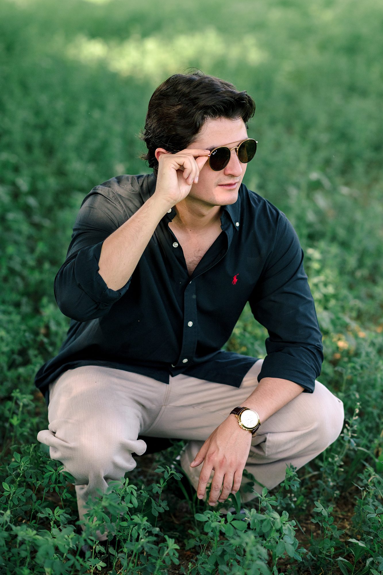 Groom-to-be crouching in an alfalfa field adjusting his sunglasses, editorial engagement portrait in northern Mexico — David Lack